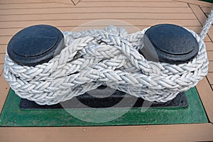 Black paired metal bitts posts with ship rope twisted on it, installed on board of  vessel on  green pedestal on ship deck