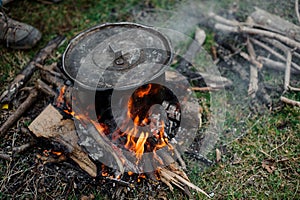 Black pan with a cover standing on the bonfire in the forest