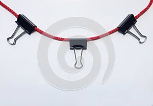 Black paper binder clip hanging on red rope isolate on white background