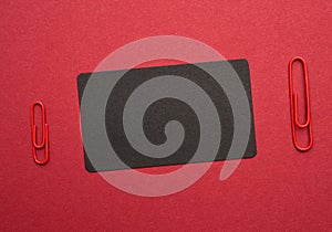 Black paper cardboard business card and red metal paper clip on a red background