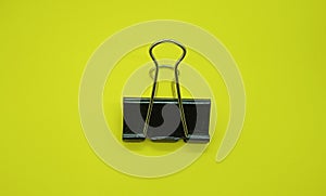 Black paper clip isolated on yellow background. Black metal paper clip.