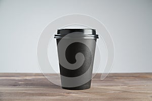 Black Paper coffee cup disposable for take away or to go, at wooden table, space for design layout.