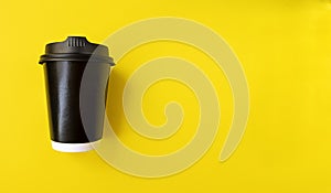 Black paper coffee cup to go on a yellow backgroud. Simple flat lay with copy space. Minimal concept. Stock photo