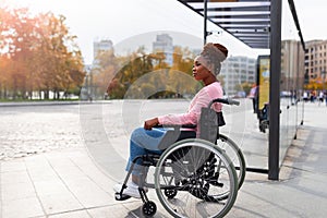 Black paraplegic woman in wheelchair waiting on bus stop, cannot board vehicle suitable for handicapped persons