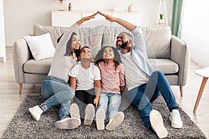 Black parents making symbolic roof of hands above children photo