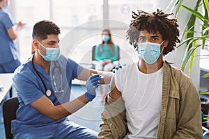 Black Patient Receiving Vaccine Injection Sitting With Doctor At Clinic