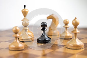 Black pawn surrounded by white chess pieces