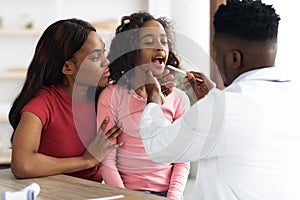 Black pediatrician checking patient little girl throat