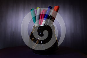Black pencil holder with colored markers and dark background photo