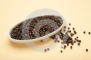 Black pepper corns in white plate on beige background. Vertical photo