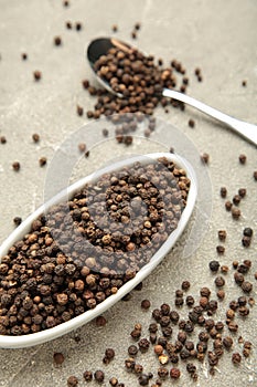 Black pepper corns in white plate on grey concrete background. Vertical photo