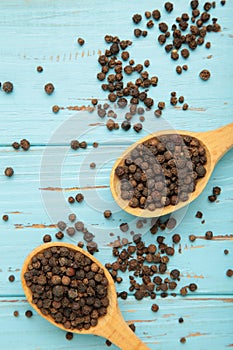 Black pepper corns in wooden spoon on blue wooden background. Vertical photo