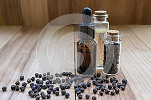 Black pepper essential oil bottle with black pepper seed, on wooden board