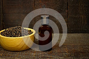 Black pepper essential oil on wooden background.