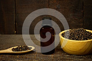 Black pepper essential oil on wooden background.
