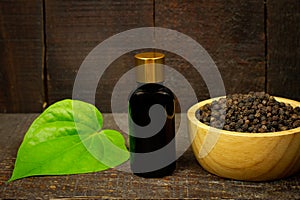 Black pepper essential oil on wooden background.