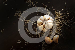 Black pepper, Garlic and rosemary on wooden plate on black background. Delicious Fresh and dried herb for steaks on wooden table.