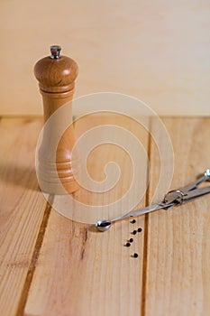 Black pepper grains and pepper grinder close up on wooden neutral background