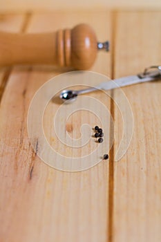 Black pepper grains and pepper grinder close up on wooden neutral background