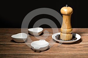 Black pepper mill with peppercorns on a white ceramic plate