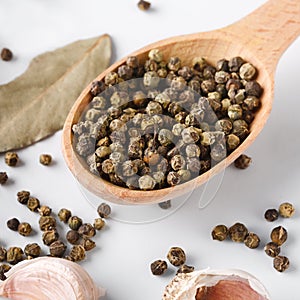 Black pepper in wooden spoon with garlic and bay leaves