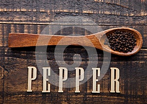 Black pepper on wooden spoon with letters below