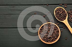 Black peppercorns in wooden bowl and spoon on black wooden background. Space for text