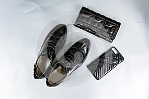 Black perforated shoes oxfords, a purse and a phone case on a paper white background