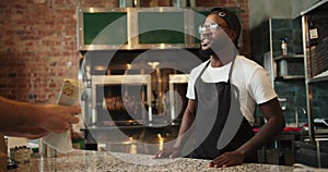 The Black person gives the order to the visitor. Fast food worker in glasses smiling and serving a visitor