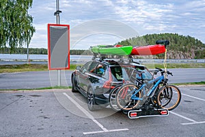 Black personal car with two mounted mountain bicycles at back side and two kayaks at top. Green and red kayaks.