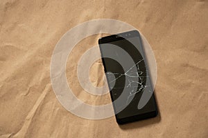 Black phone with a cracked screen on a brown background close-up