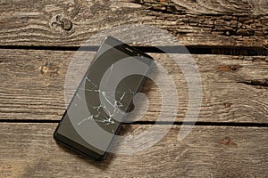 Black phone with a cracked screen on a wooden background close-up