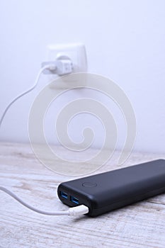 Black phone power bank plugged in the socket on the wall for charging on wooden background
