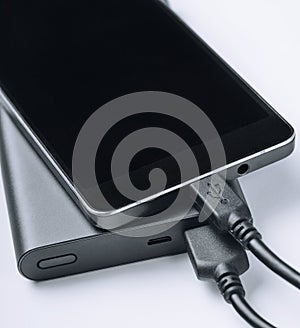 Black phone smartphone charging from power bank on white background. Modern technology concept.