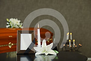 Black photo frame with burning candle and  lily on table in funeral home