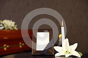 Black photo frame with burning candle and white lily on table