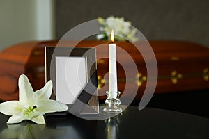 Black photo frame with burning candle and white lily on table