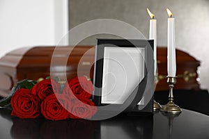 Black photo frame with burning candles and red roses on table