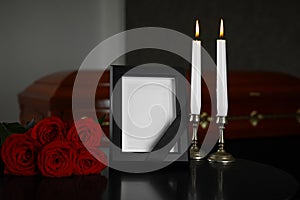 Black photo frame with burning candles and red roses on table