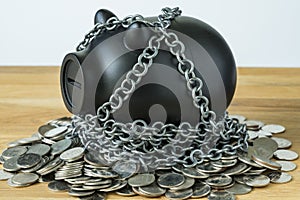 Black piggy bank with chains on top of coins as security protect