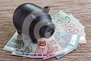 Black piggy bank on pile of Euro banknotes on wooden table, financial savings money account concept, future growth of interest co