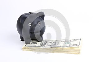 Black piggy bank standing on stack of money american hundred dollar bills on white background