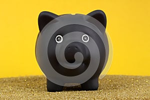 Black piggy bank standing on yellow, gold sand in front of yellow background