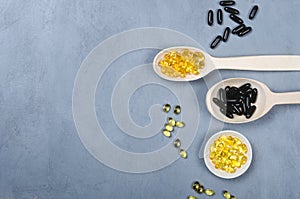 Black pill, yellow pill and wooden spoon on grey background