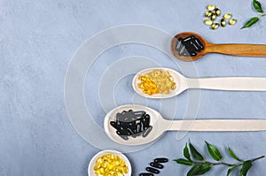 Black pill, yellow pill and wooden spoon on grey background