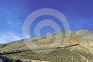 Black pipeline runs across desert valley and up hillside under a blue sky