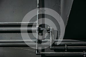 Black pipes on dark wall background as abstract industrial pipeline texture