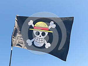 Black pirate flag which contains a white skull with a yellow straw hat and a red ribbon located on two white bones