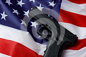 A black pistol lies against the background of the American flag. Personal weapons of the population. Close-up