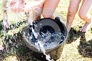 Black plastic bucket with fresh water with many kids legs playing summer games